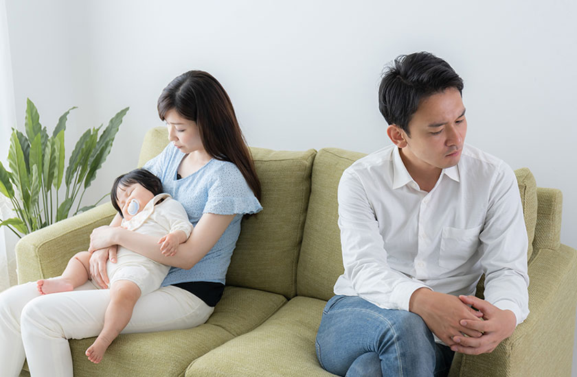 離れて座る夫と赤ちゃんを抱き抱える妻